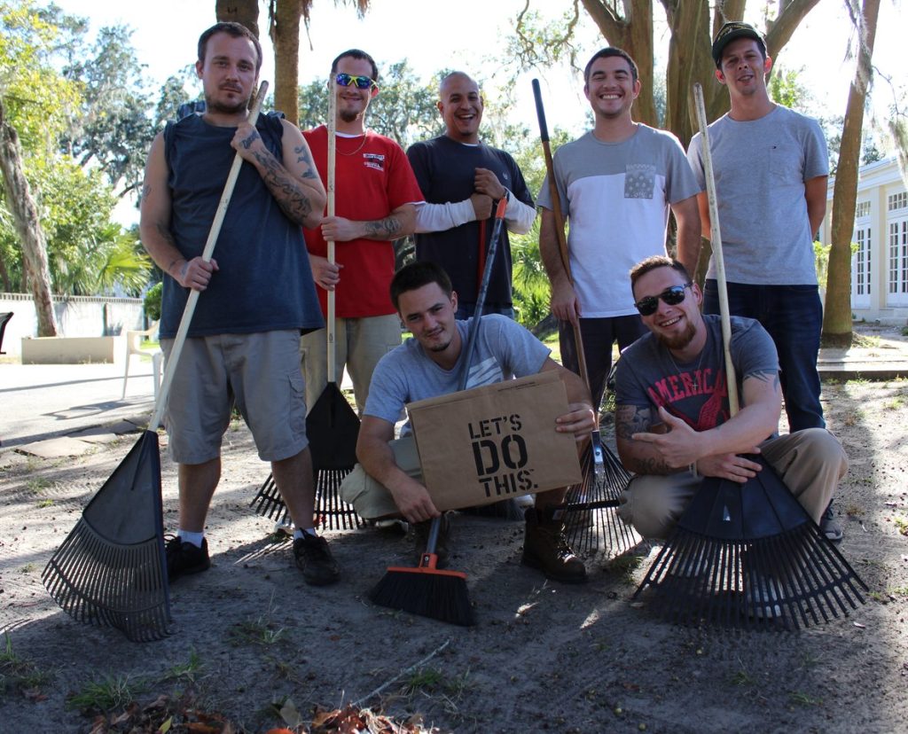 Residents with rakes and a Let’s Do This sign during a yard work project at the Savannah Mission